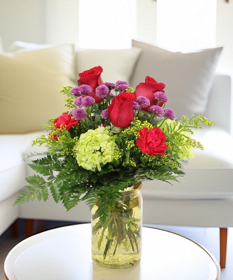 Bright Days bouquet with hydrangea, pink carnations, and purple button poms in a hammered glass vase. A cheerful Mother’s Day gift.