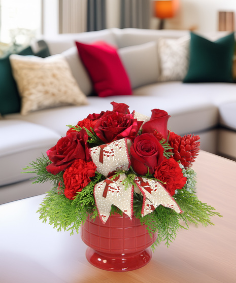 Holiday bouquet in red footed pot with evergreens, red carnations & Panther roses. Festive arrangement with red pinecones and cardinal ribbon