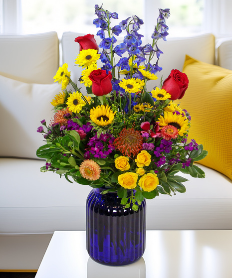Sunflowers, delphinium, protea, and viking poms in a cobalt blue ridged vase. A rich and abundant Mother's Day gift she will treasure