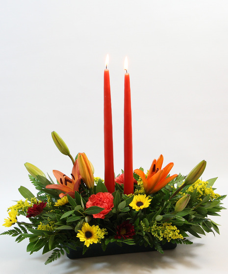  Two tapered candles nestled among orange Asiatic lilies, carnations, bronze daisy poms, and sunny yellow Viking poms. 