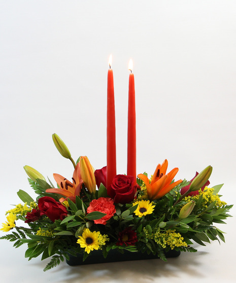  Two tapered candles nestled among orange Asiatic lilies, carnations, bronze daisy poms, and sunny yellow Viking poms. 