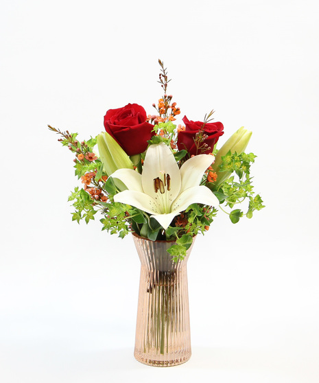 This delightful arrangement features two stems of pristine white Asiatic lilies accompanied by graceful accents, all presented in a charming colored vase. 