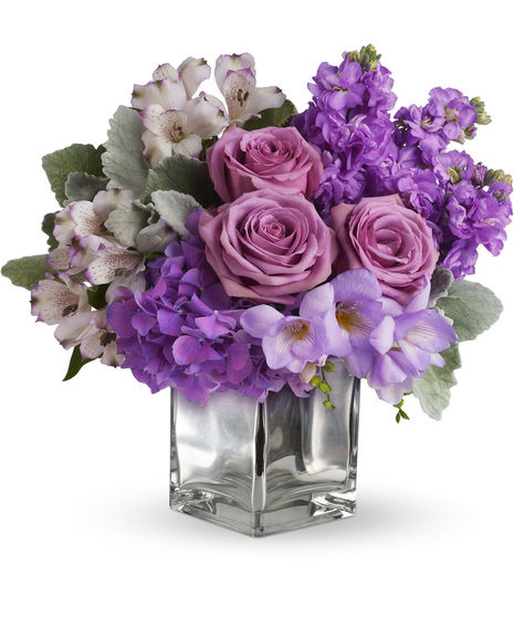 Lush lavenders, frosty whites and silvery greens look inside a cool cube vase. Arrangement is in an icy, clear glass cube vase.
