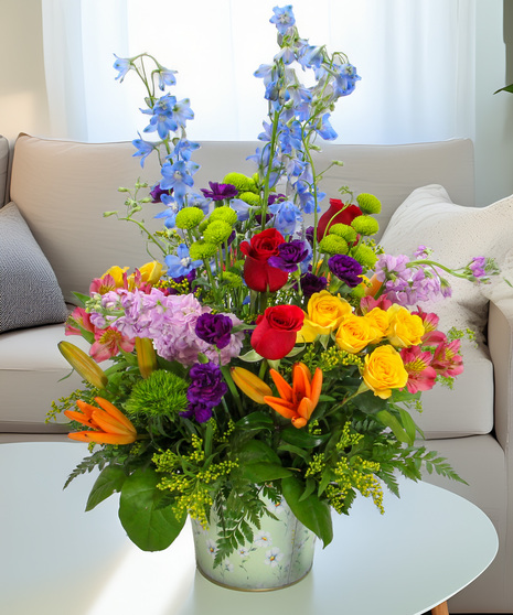 An abundant mix of delphinium, stock, spray roses, and lilies in a floral tin. A vibrant and heartfelt Mother's Day gift she will love.