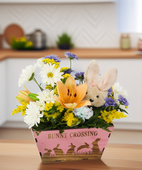 A playful Easter bouquet of lilies, daisies, and rainbow carnations in a bunny silhouette wooden box. A charming gift for the whole family.