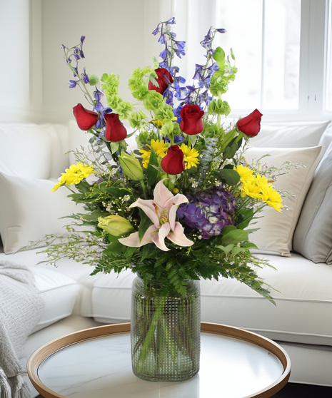 Oriental lilies, bells of Ireland, delphinium, hydrangea, and daisies in a colored glass vase. A sweeping floral arrangement that feels like art