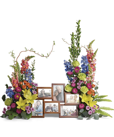 An awe-inspiring accent for your beloved photos at the service, this lush rose, lily and delphinium bouquet reflects a colorful life full of radiant memories.