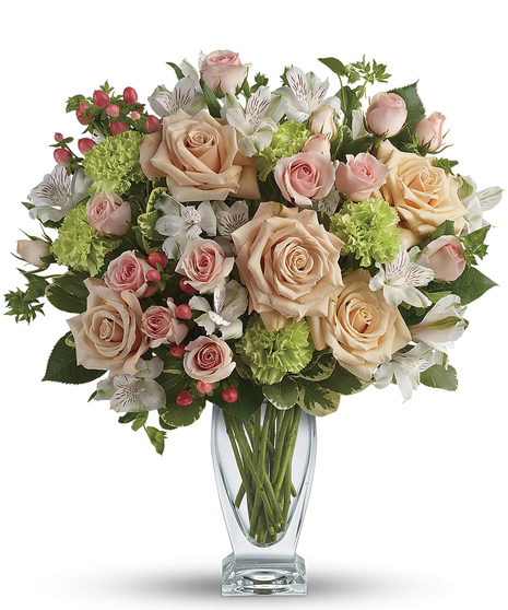 Beautiful peach roses and spray roses, white alstroemeria, brilliant green carnations, peach hypericum and fresh garden greens are perfectly hand-arranged in a vase. 